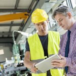 Supervisor and manual worker using digital tablet in metal industry